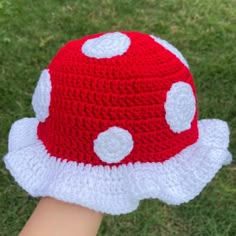 a red and white crocheted mushroom hat on someone's hand in the grass