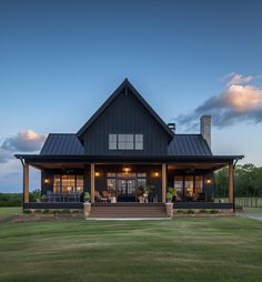 a large house with a porch and covered in windows at dusk, sitting on the grass