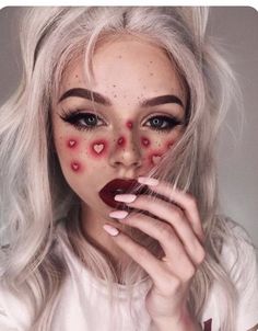 a woman with white hair and red makeup is holding her hands to her face while she has