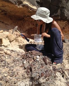 a woman sitting on top of a pile of rocks next to a shovel and water bottle