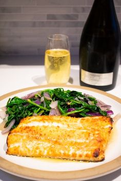 a white plate topped with fish next to a bottle of wine and a glass of wine