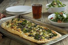 a pizza sitting on top of a metal pan next to bowls of salad and drinks