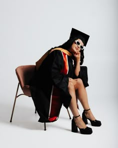 a woman in graduation gown sitting on a chair with her legs crossed and holding a cell phone to her ear