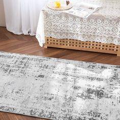 a white and gray area rug on a wooden floor next to a window with curtains