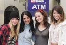 four young women standing together in front of a atm