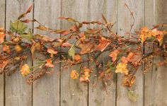 an arrangement of flowers and leaves on a wooden fence