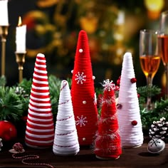 christmas trees made out of yarn sitting on a table next to wine glasses and candles