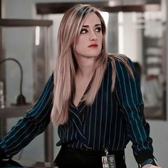 a woman with long blonde hair wearing a black and white striped shirt is sitting at a desk