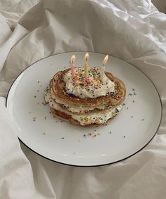 a stack of pancakes topped with white frosting and lit candles on top of a plate