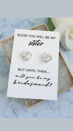 a pair of silver earrings sitting on top of a card next to a white rose