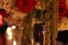 red and white flowers are in vases on the table with candles behind them at a party