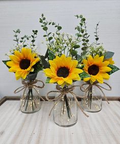 three vases with sunflowers and greenery tied to them on a table