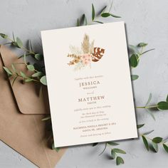 an elegant wedding card with leaves and flowers on the front is displayed next to two envelopes