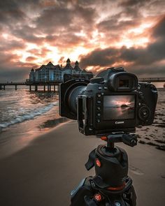 a camera is set up on a tripod at the beach as the sun sets