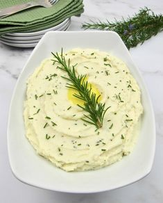 mashed potatoes in a white bowl with a sprig of rosemary on top