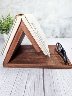 an open book sitting on top of a wooden stand next to a pair of glasses