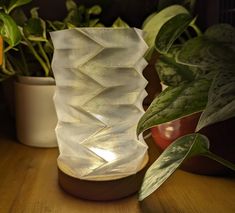 a white vase sitting on top of a wooden table next to some potted plants