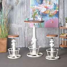 three white pedestals with wooden tops in front of a painting and potted plant