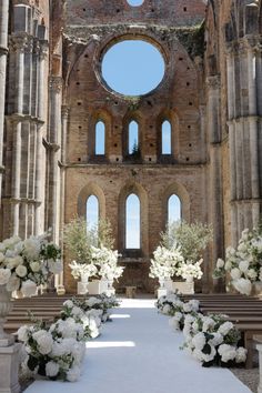 the aisle is decorated with white flowers and greenery in front of an old building