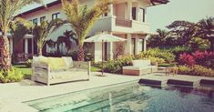 a house with a swimming pool and palm trees in the front yard, surrounded by lush greenery