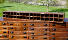 an old wooden dresser with many drawers and knobs on it's sides in front of a grassy area