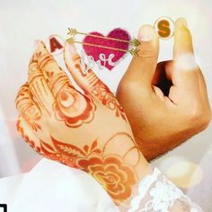 two hands with henna tattoos holding an arrow and a heart shaped brooch pin