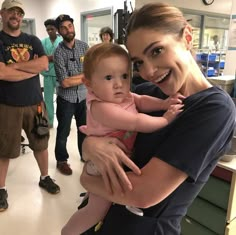 a woman holding a baby in her arms while standing next to other men and women