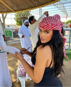 a beautiful woman in a black dress holding a piece of paper while standing next to other people