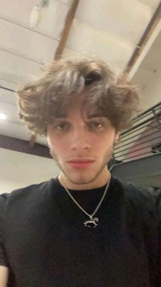 a young man with curly hair wearing a black t - shirt is taking a selfie