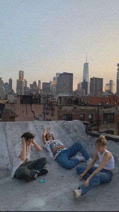 two women sitting on the ground in front of a skateboard ramp with cityscape in the background