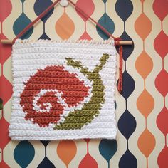 a crocheted square hanging on a wall with an orange and white flower design