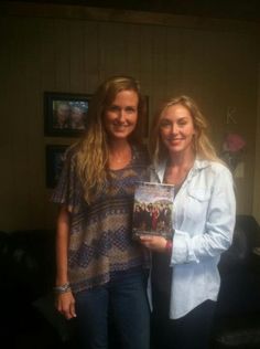 two women standing next to each other holding a book