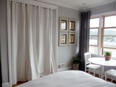 a white bed sitting in a bedroom next to a window with curtains on top of it