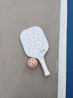 a ping pong paddle with a pink ball on the ground in front of it