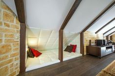 a bedroom with exposed brick walls and wood flooring, along with a bed that has red pillows on it