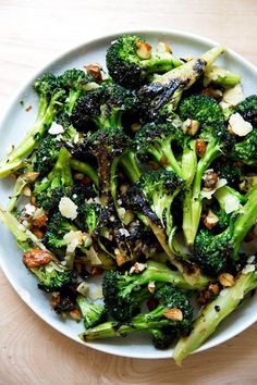 a white bowl filled with broccoli and nuts on top of a wooden table