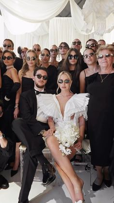 a group of people sitting next to each other in front of a white curtain and wearing sunglasses