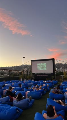 people sitting on bean bag chairs in front of an outdoor movie screen at dusk with the sun setting behind them