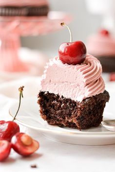 a piece of chocolate cake with pink frosting and cherries on the plate next to it