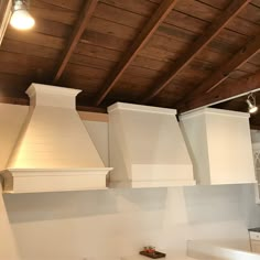 a kitchen with white appliances and wood ceilinging on the walls, along with an open stove hood