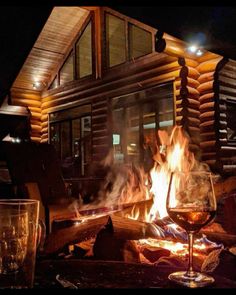 a glass of wine sitting on top of a fire pit in front of a log cabin