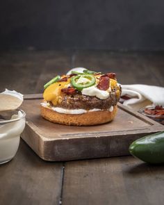 an open face sandwich on a wooden cutting board next to some sauces and peppers