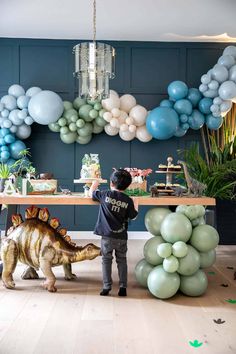 a young boy standing in front of a table with balloons on it and an adult dinosaur