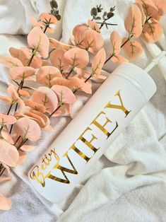 pink flowers are placed next to a white travel mug with the word whey written on it