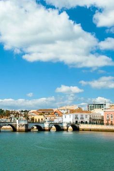 a bridge over the water with buildings in the background and clouds in the sky above