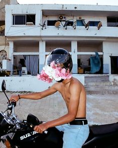 a shirtless man on a motorcycle with flowers in his hair and wearing a helmet