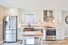 a kitchen with stainless steel appliances and wooden table in the foreground is a clock on the wall