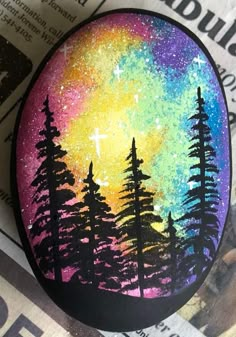 a painted rock sitting on top of a newspaper next to a tree filled sky with stars