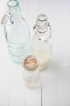 two empty glass bottles sitting next to each other on a white wooden table with one bottle filled with milk