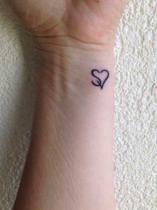 a small tattoo on the wrist of a person with a heart and two letters in it